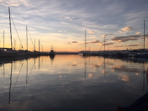 Un puerto deportivo con varios veleros amarrados, agua tranquila y un atardecer al fondo.