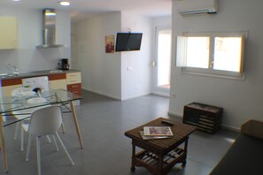 Una cocina moderna con una mesa de comedor de vidrio, sillas blancas y una pequeña mesa auxiliar de madera con una revista.