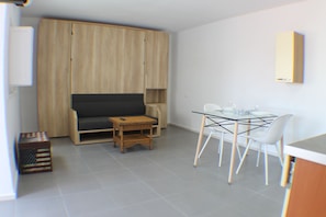 Un espacio habitable compacto con un sofá, una mesa de comedor con sillas, una pequeña mesita auxiliar y un armario.