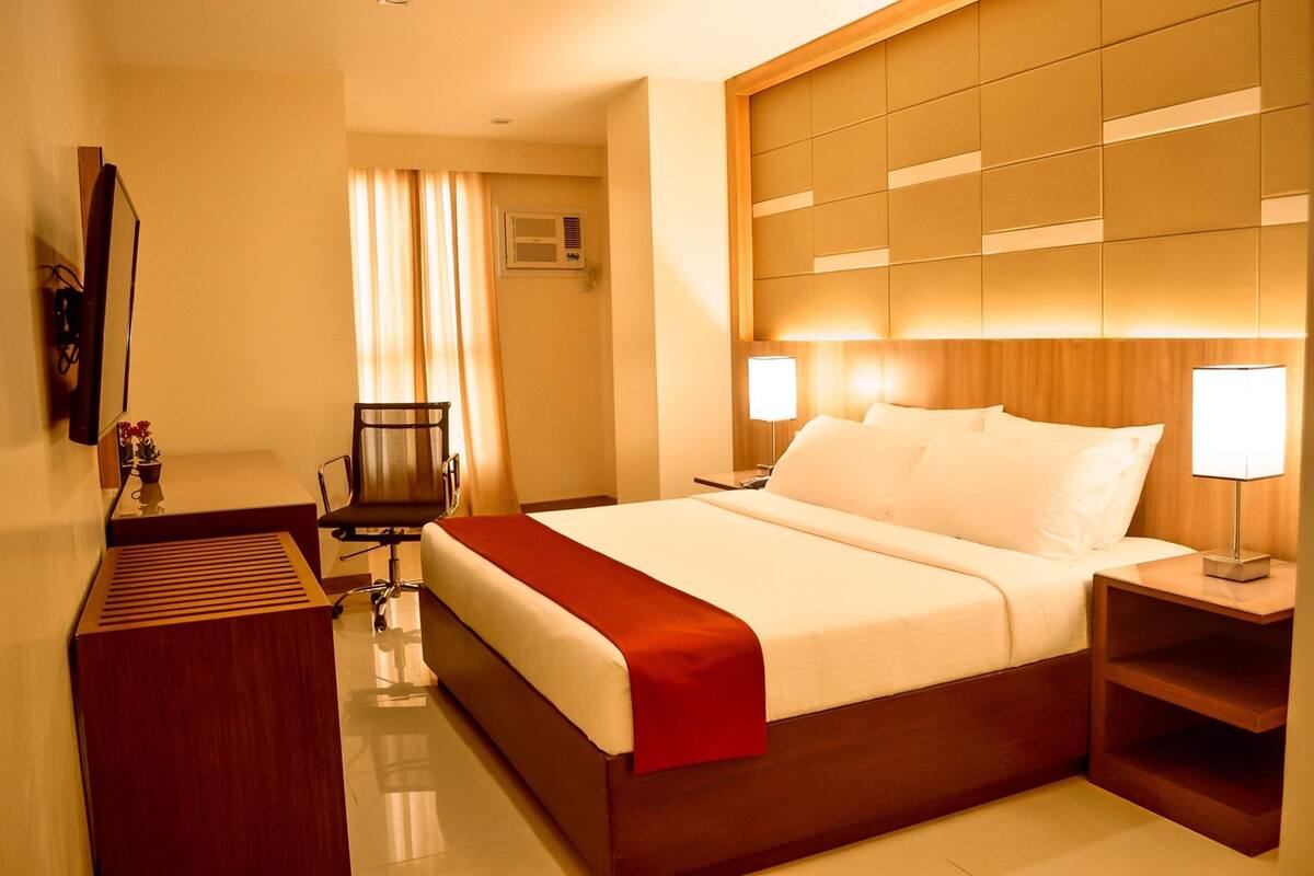 A hotel room with a large bed, bedside lamps, a desk with a chair, and a mirror.