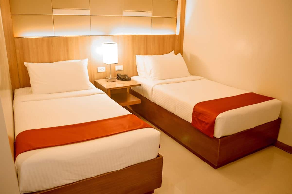 A hotel room with two single beds, a nightstand with a lamp, and a wooden headboard.