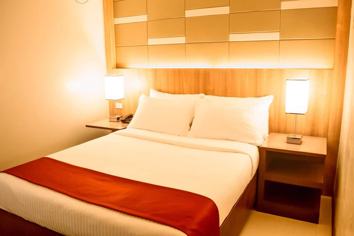 A hotel room with a large bed, two bedside tables with lamps, and a wooden headboard.