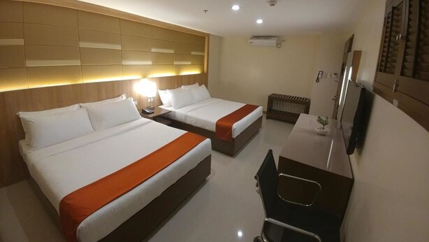 Habitación de hotel con dos camas, un escritorio, una silla, un televisor y un cabecero con iluminación integrada.