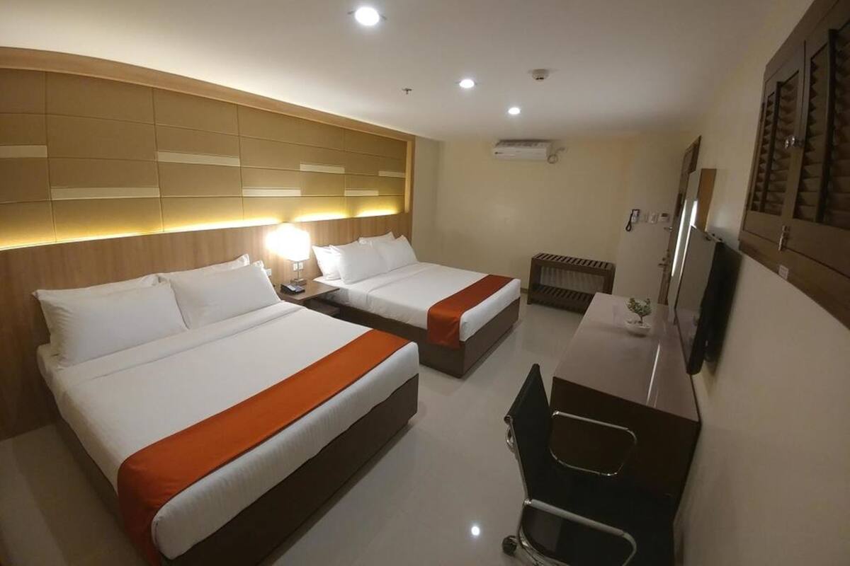 A hotel room with two beds, a desk, a chair, a TV, and a headboard with built-in lighting.