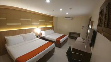 A hotel room with two beds, a desk, a chair, a TV, and a headboard with built-in lighting.
