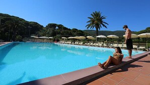 A swimming pool with lounge chairs and umbrellas, surrounded by greenery and hills. - Studio - Studio Apartment, Sleeps 4 (Porto Azzurro)