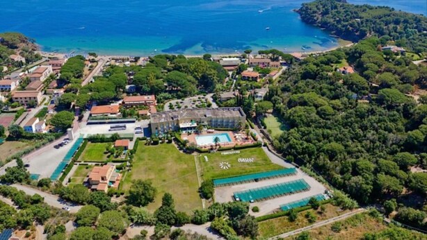 An aerial view of a coastal property with a swimming pool, tennis courts, and a large building with a garden. - Studio - Studio Apartment, Sleeps 4 (Porto Azzurro)