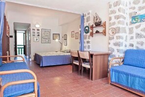 A room with two beds, a table, chairs, a wall clock, and a stone wall.