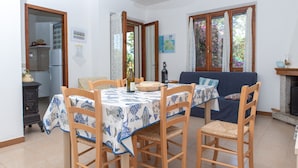 Ein Essbereich mit einem Tisch, gedeckt für vier Personen, Holzsesseln, einer blau-weißen Tischdecke und einer blauen Couch im Hintergrund.