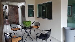 Uma área de varanda coberta com quatro cadeiras, uma mesa, um vaso de planta e uma lixeira.