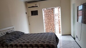 Quarto com cama, guarda-roupa e porta que dá para uma parede de pedra.