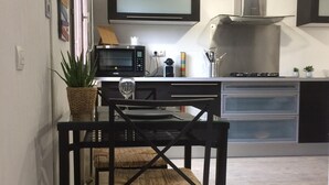 Een kleine keuken met een magnetron, fornuis en een eethoek met een tafel en stoelen.
