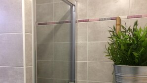 Een badkamer met een douche, een houten bankje en een potplant.