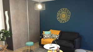 Een moderne woonkamer met een donkerblauwe muur, een zwarte bank, een gele salontafel en een klein krukje.