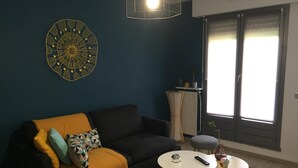 Een woonkamer met een donkerblauwe muur, een zwarte bank met een gele deken, een ronde witte salontafel en een kleine ronde tafel met een afstandsbediening.