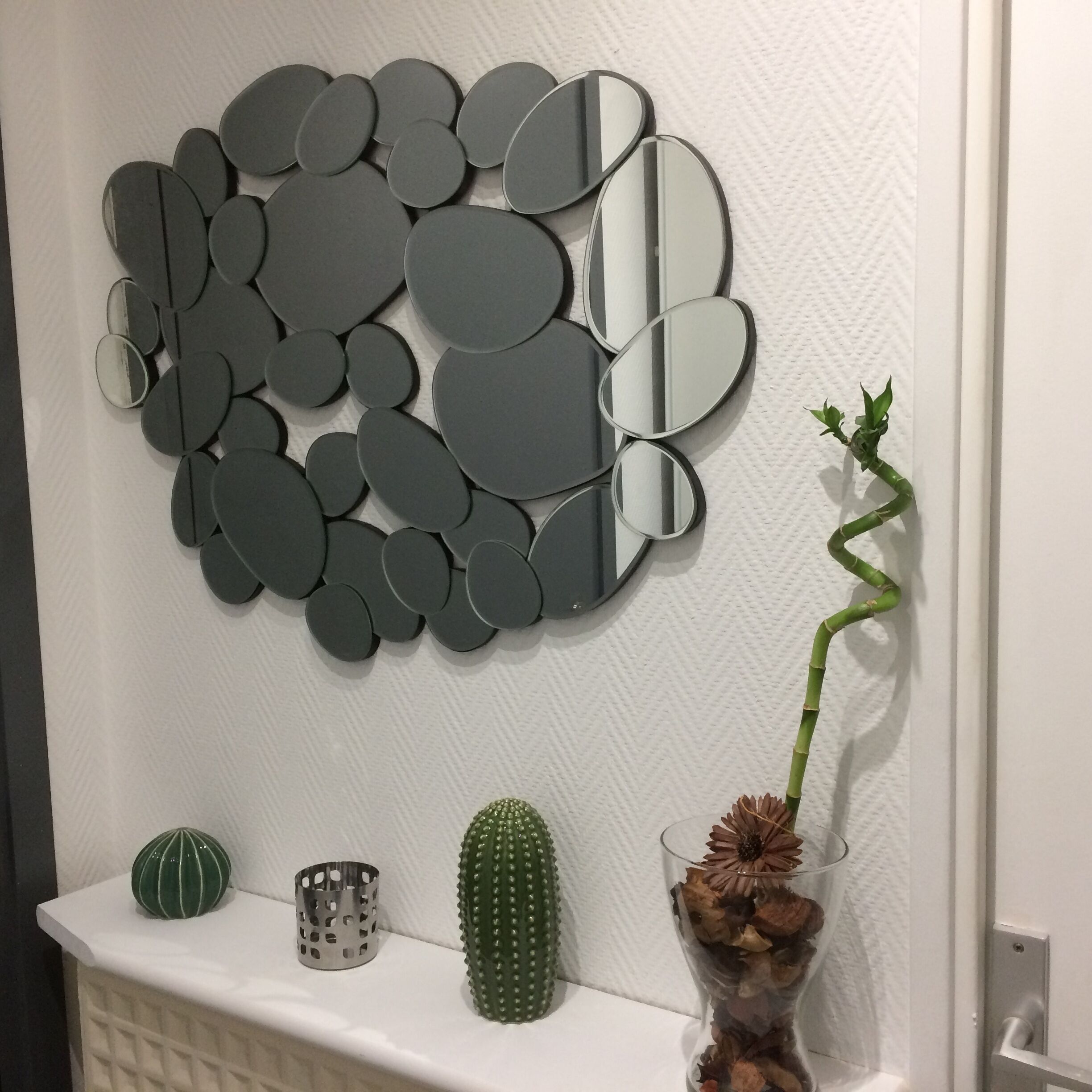 En vägg med ett mosaikmönster av spegelbitar, en kaktus och en vas med torkade blommor.