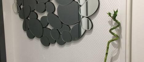 En vägg med ett mosaikmönster av spegelbitar, en kaktus och en vas med torkade blommor.