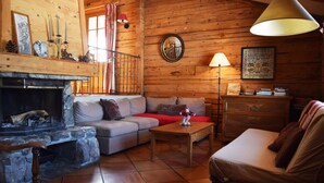 Un acogedor interior de cabaña de madera con chimenea, un sofá, una mesa de centro y una lámpara.