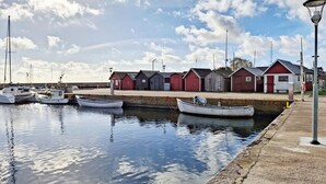 En lystbådehavn med fortøjede både, en ankomstbro og flere små bygninger med røde og grå facader.