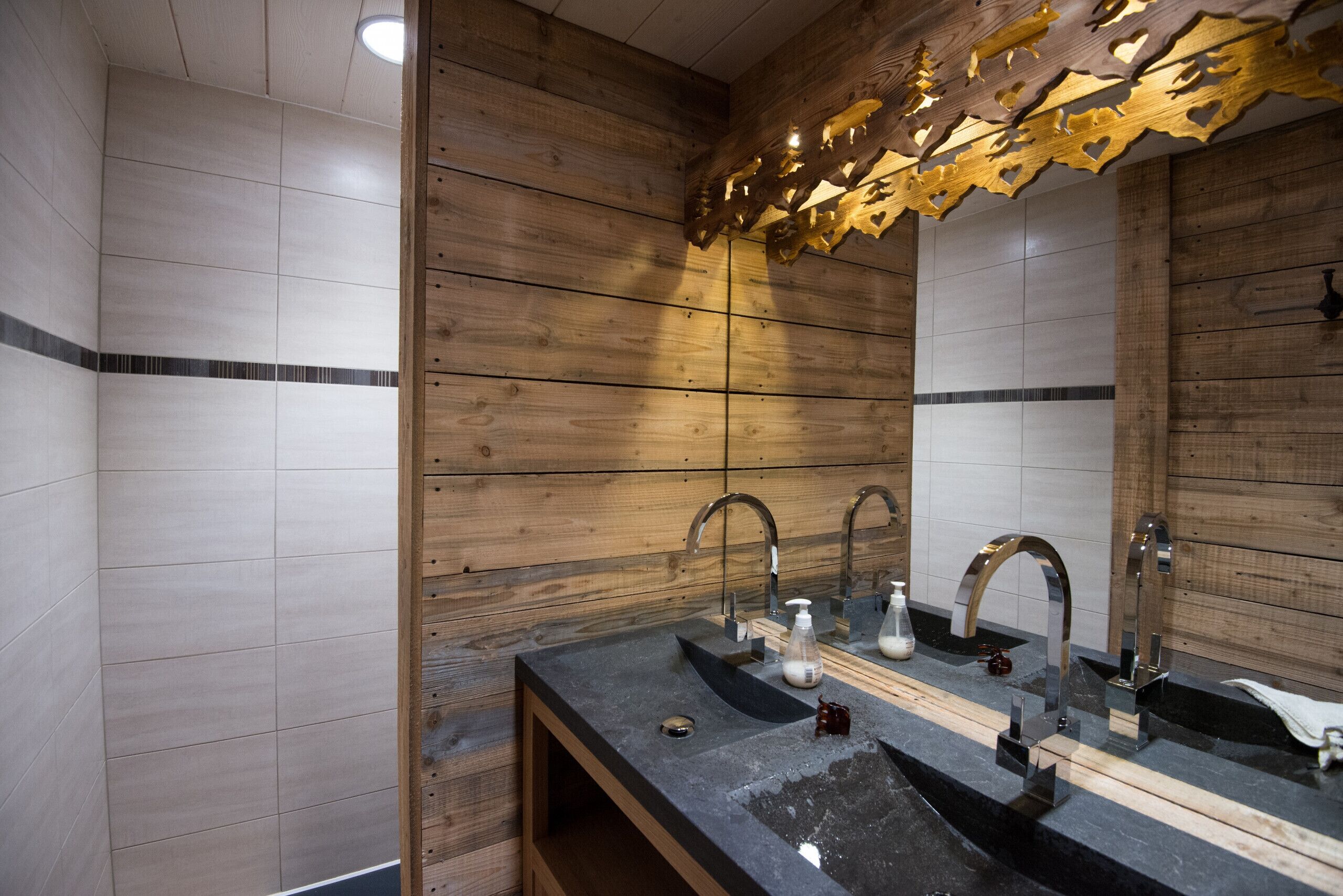 A modern bathroom with wooden panel walls, a large mirror, and a dual sink with faucets.