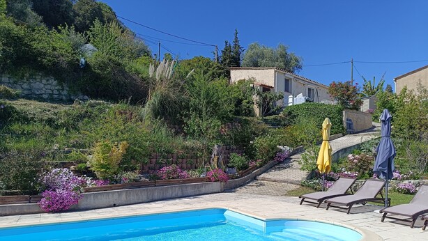 A swimming pool with lounge chairs and umbrellas, surrounded by lush greenery and a stone wall.