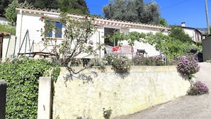 A building with a tiled exterior, a visible door, and a small garden area with flowering plants.