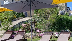A patio area with lounge chairs and umbrellas, surrounded by a garden with various plants and flowers.