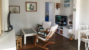 A living room with a wooden rocking chair, a glass-top coffee table, a television, and various wall decorations.