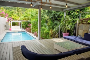 A pool area with a wooden deck, a lounge chair, and a glass table.