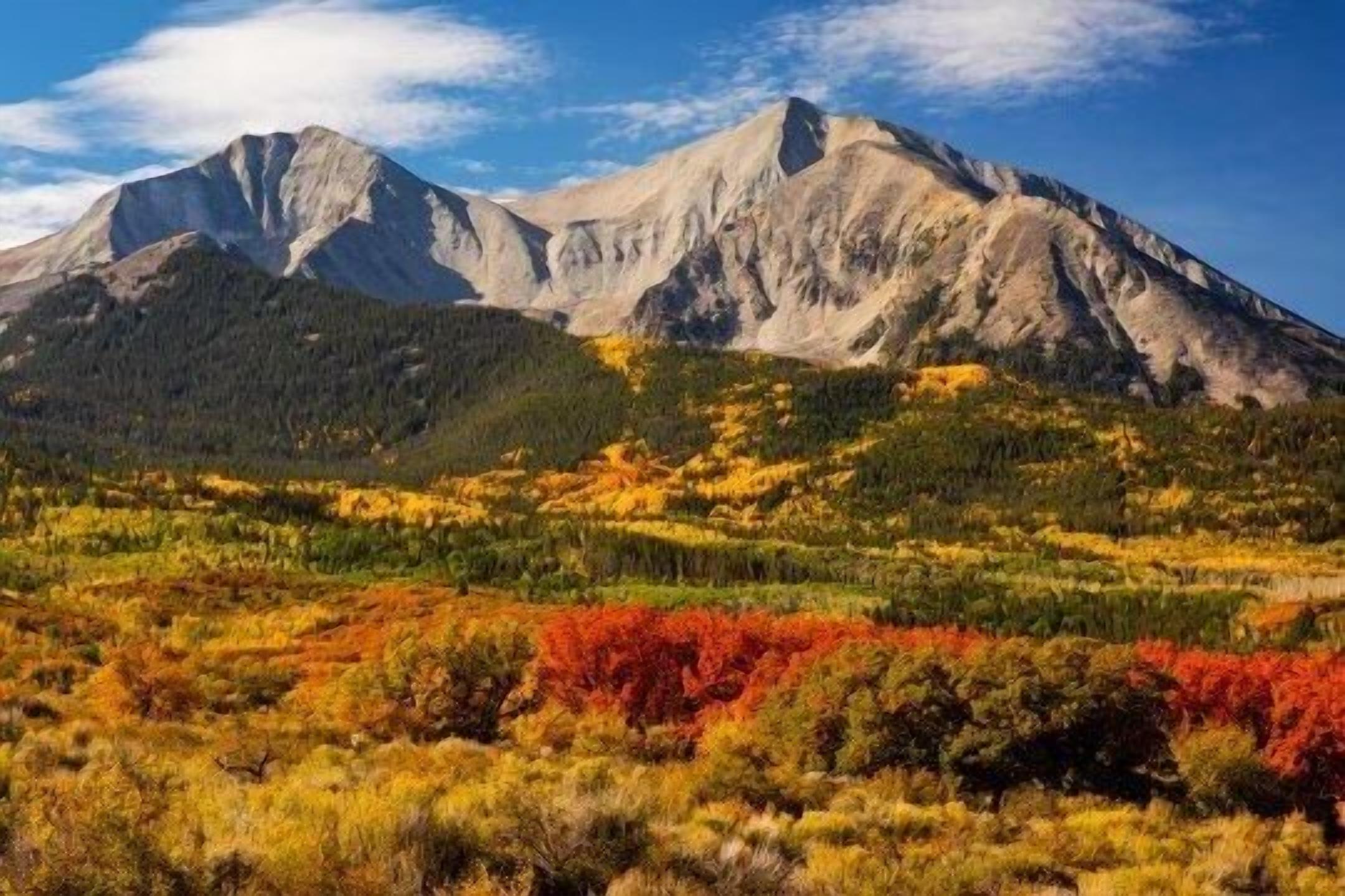 Un paysage montagneux avec un sommet imposant, des zones boisées et un feuillage aux couleurs automnales.