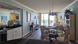 A spacious living area with a dining table, comfortable seating, and a view of the outdoors. - The Pearl #304 - FREE BEACH SETUP March-October! (Navarre Beach)