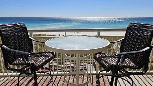 A balcony with a round table and two chairs, overlooking a beach and ocean. - The Pearl #304 - FREE BEACH SETUP March-October! (Navarre Beach)