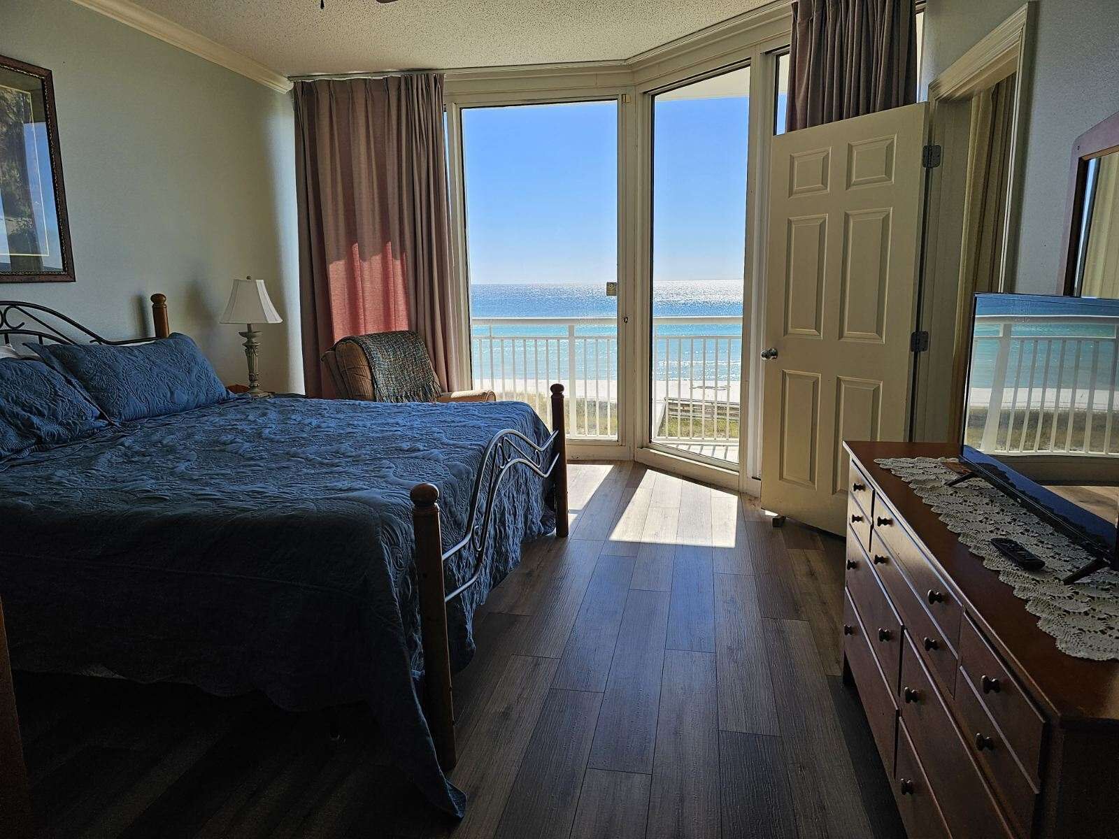 Une chambre à coucher comprenant un lit, une chaise, une commode et une grande fenêtre donnant sur l’océan.
