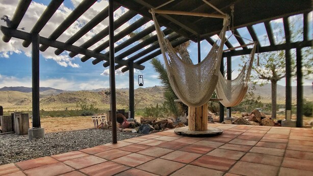 Eine Hängematte unter einer Holzw pergola, eine gemusterte Matte und eine Schildkröte auf dem Boden.