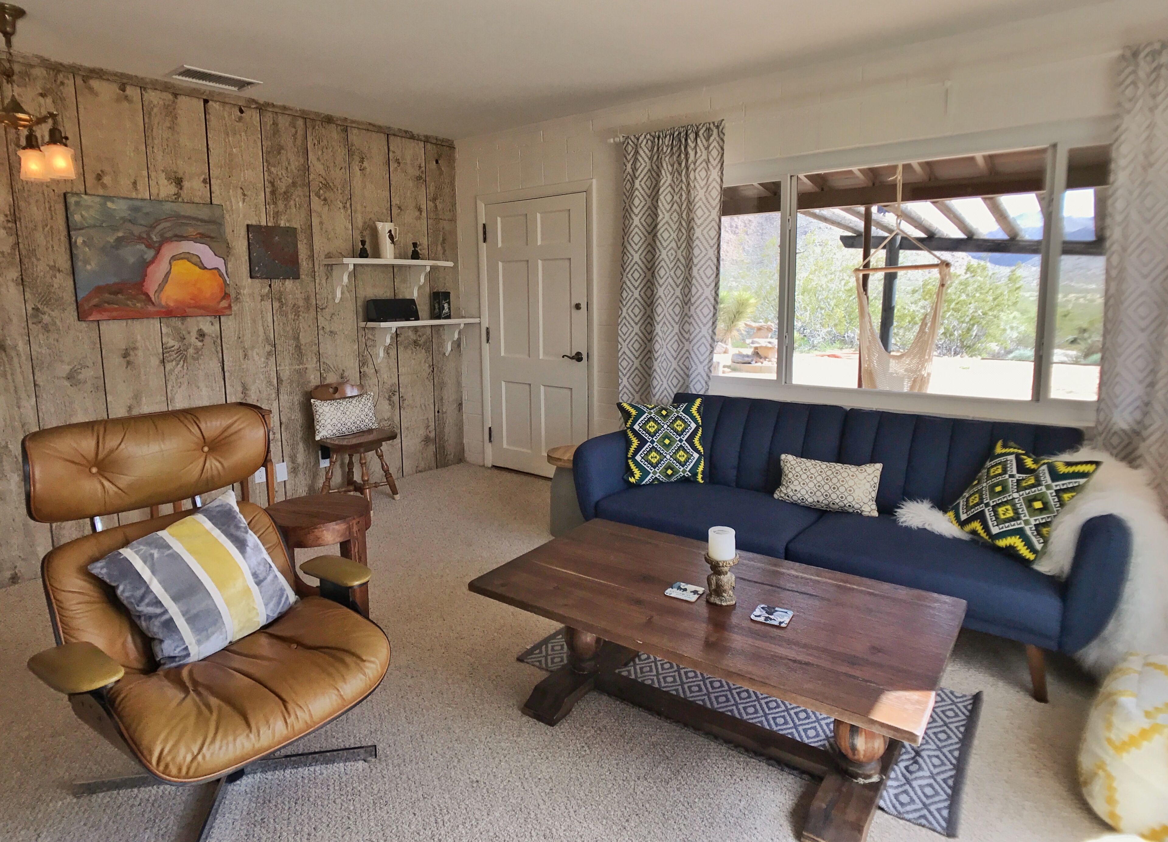 A cozy living room with a brown leather chair, a blue sofa with patterned cushions, a wooden coffee table, and a white door.