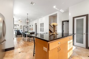 A modern kitchen with a central island, wooden cabinets, and a dining area with chairs.