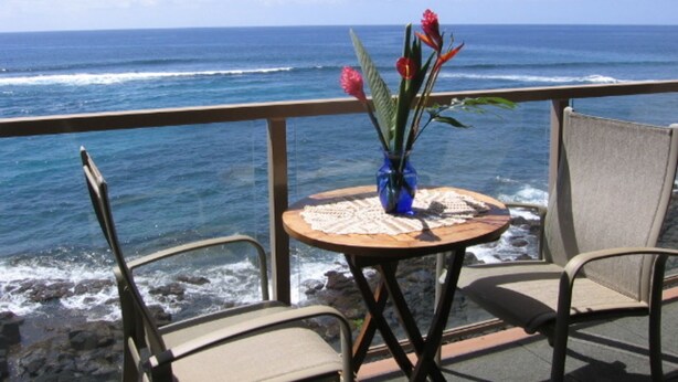 A table with a vase of flowers and two chairs on a balcony overlooking the ocean. - Live TOP Floor OceanFRONT. Relax & Sleep to Sounds of the Surf; AC or Tradewinds (Koloa)