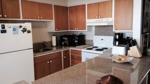 A kitchen with wooden cabinets, a granite countertop, a stove, a refrigerator, and a coffee maker. - Live TOP Floor OceanFRONT. Relax & Sleep to Sounds of the Surf; AC or Tradewinds (Koloa)