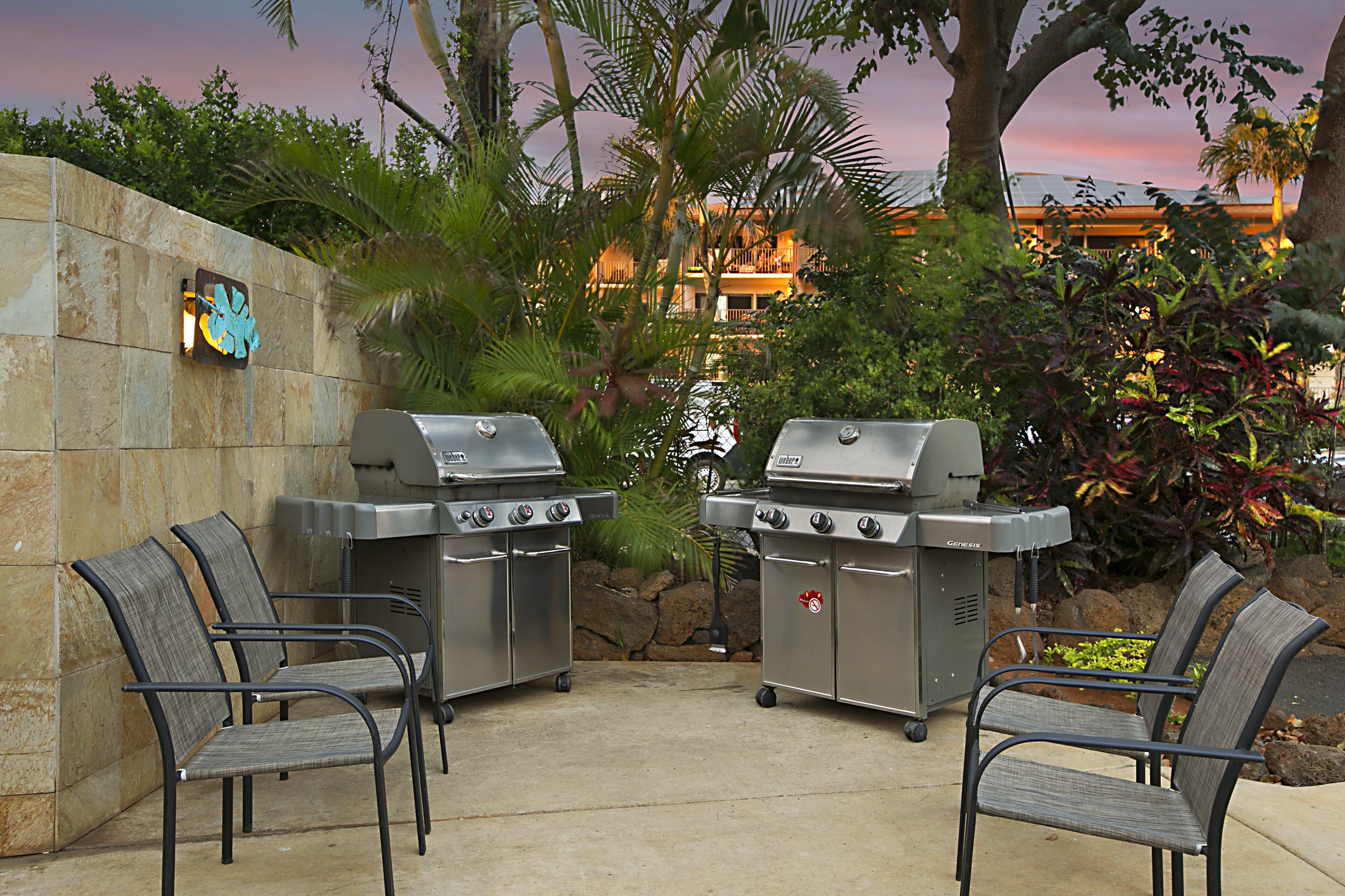 Two barbecue grills, two chairs, and a stone wall with a decorative sign.