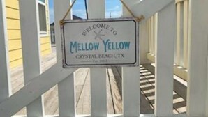 Een witte houten omheining met een bord waarop staat: Welkom bij Mellow Yellow Crystal Beach, TX.