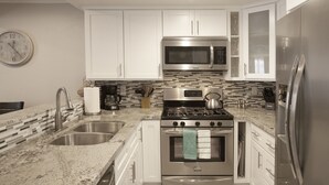 A modern kitchen with stainless steel appliances, white cabinets, and a tiled backsplash. - Walk To Disneyland, Disneyland Rental Home 2. (Anaheim)