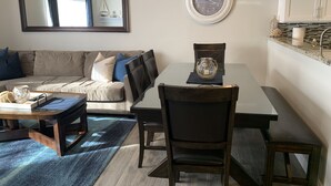 A living room with a sofa, coffee table, and chairs, a dining table with a clock, and a kitchen area with cabinets and a sink. - Walk To Disneyland, Disneyland Rental Home 2. (Anaheim)