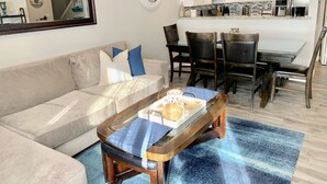 A living room with a sofa, coffee table, and dining area with chairs. - Walk To Disneyland, Disneyland Rental Home 2. (Anaheim)