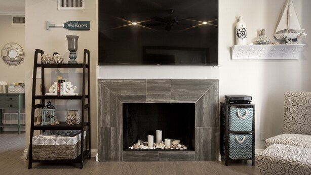 A living room with a fireplace, a television mounted above it, a bookshelf, and a patterned armchair. - Walk To Disneyland, Disneyland Rental Home 2. (Anaheim)