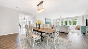A dining area with a wooden table, white chairs, and a vase of yellow flowers. - 92 Reviews, 10-Star ☀️ 1 House from Gulf | Private Beach | Beach Gear | 5200 SF | 6BR ☀️ 30A (Santa Rosa Beach)