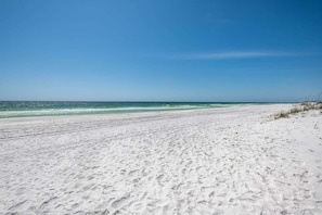 A wide sandy beach with gentle waves, clear skies, and a distant horizon.