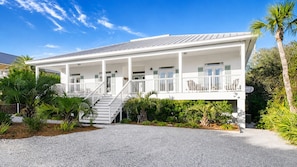 A white building with a covered porch, a staircase, and a gravel driveway. - 92 Reviews, 10-Star ☀️ 1 House from Gulf | Private Beach | Beach Gear | 5200 SF | 6BR ☀️ 30A (Santa Rosa Beach)