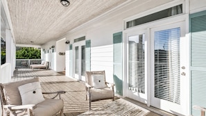 A covered porch with outdoor furniture, a sliding glass door, and a view of greenery.