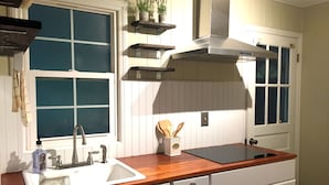 Una cocina con encimera de madera, armarios blancos y un lavamanos de acero inoxidable, además de una ventana con persianas.