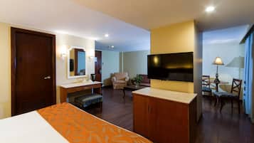 A hotel room with a bed, a desk, a TV, a chair, and a small table with a lamp.